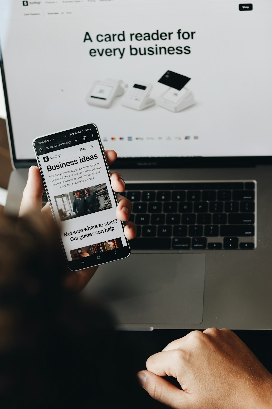 A person is holding a smartphone displaying a page on business ideas. This image emphasizes the support SumUp provides to entrepreneurs and small business owners, helping them grow and manage their payment processes seamlessly.